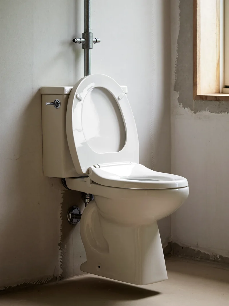 Wandhängendes Keramik-WC im Rohbau mit sichtbaren Anschlüssen, illustrativ